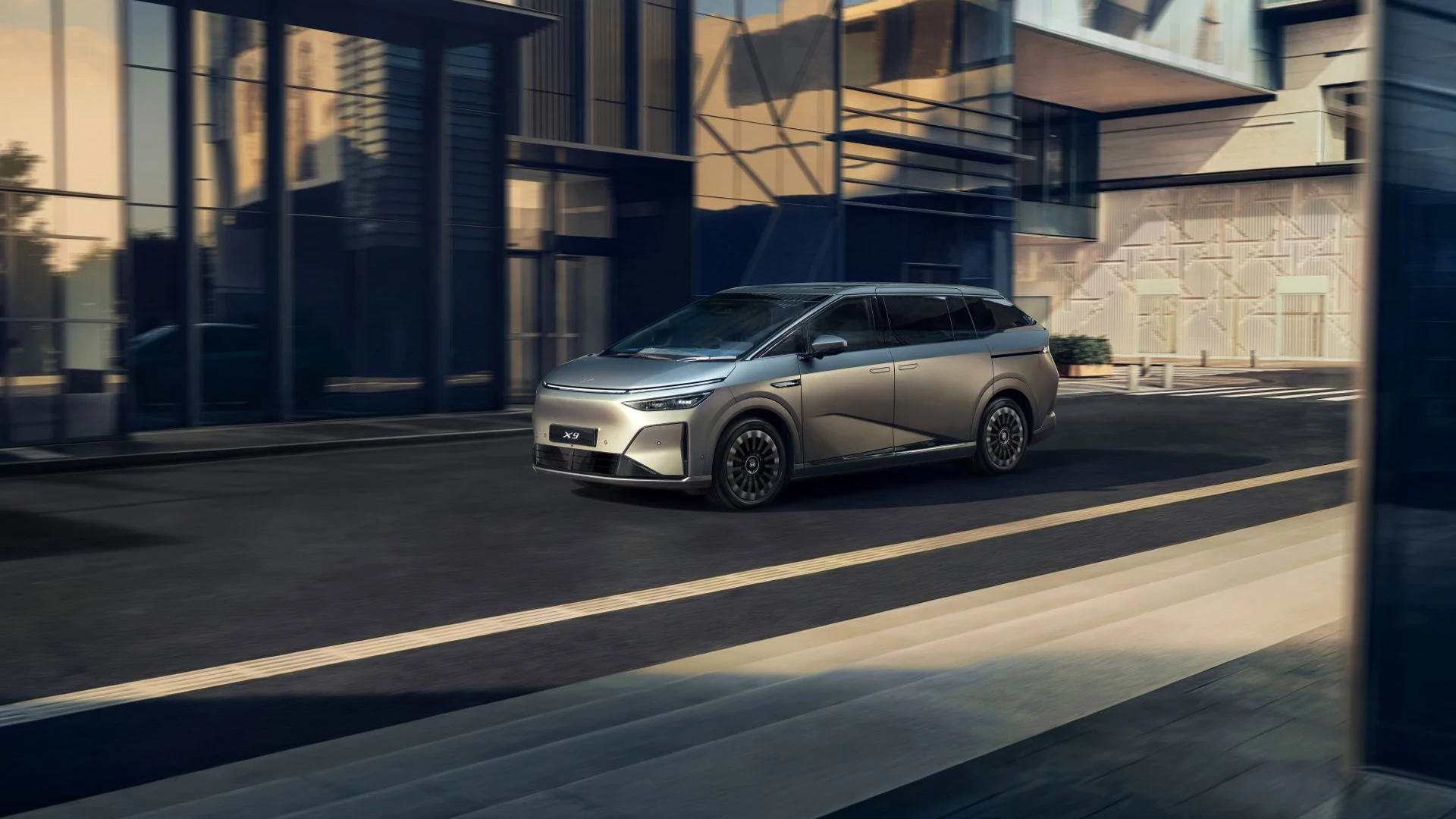 XPENG X9 driving past a modern building in the official UK launch photograph